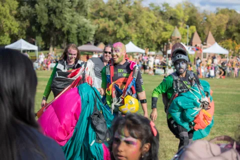 Skydivers in face paint carry canopies across the field.