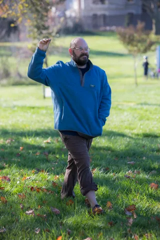 A person waves while walking across the lawn