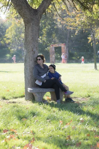 Two people rest on a bench under a wide shade tree