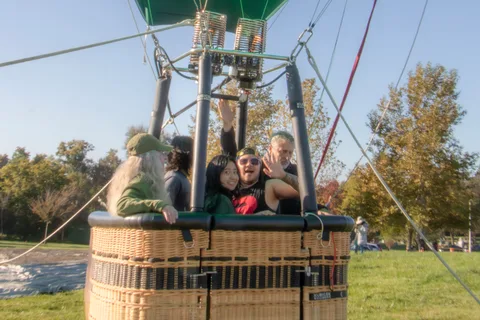 Passengers look out from a balloon basket on the ground.