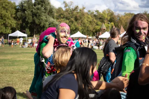 Skydivers in face paint walk the crowd line with their canopies.