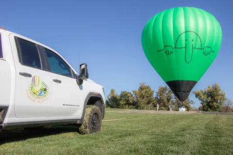 A green balloon on the field beyond a parked truck