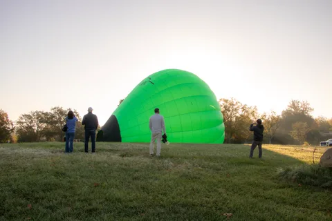 A green balloon inflates on the lawn at sunrise