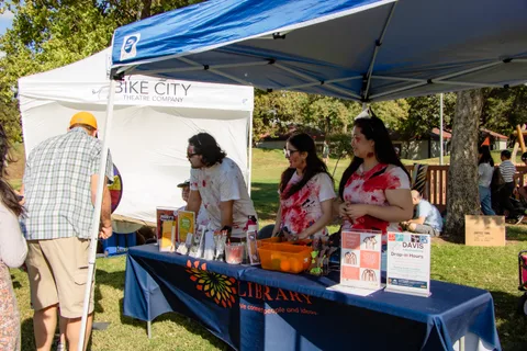 Staff hand out information at a library booth under a blue canopy.