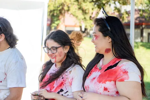 Two volunteers in blood spattered shirts talk together beside a booth.