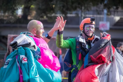 Two skydivers in face paint wave with canopies bundled up.