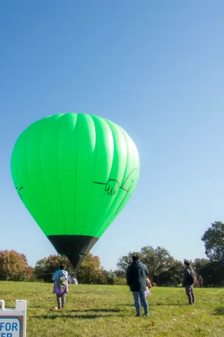 A green balloon floats over a field with two people watching