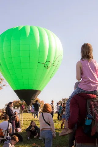 A child on shoulders watches a green balloon rise