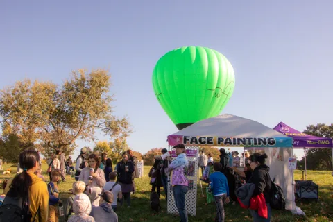 A crowd gathers by the face painting tent under a green balloon