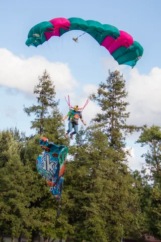 A skydiver clears the treetops with a flag hanging beneath.
