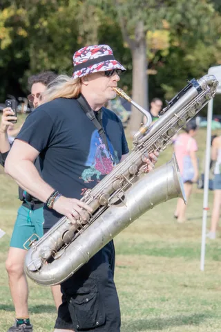 A saxophone player in a bucket hat plays in the middle of the field.
