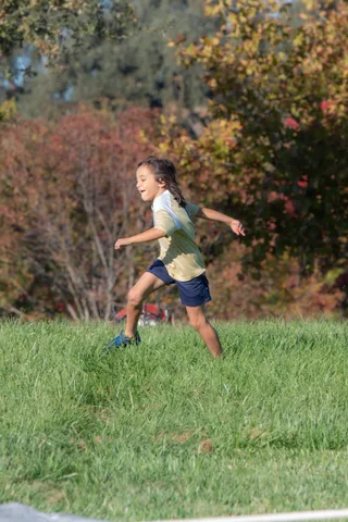 A child runs across the grass with autumn trees behind