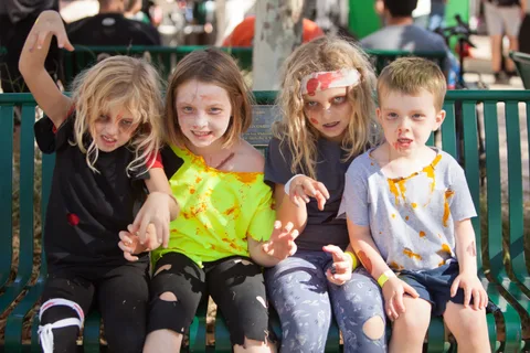Four kids in zombie makeup sit together holding hands on a bench.