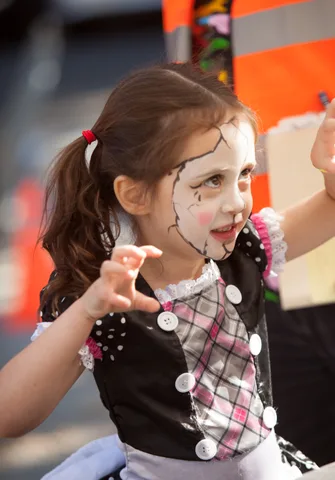 A girl in a plaid and skull-print outfit reaches out at a craft table.