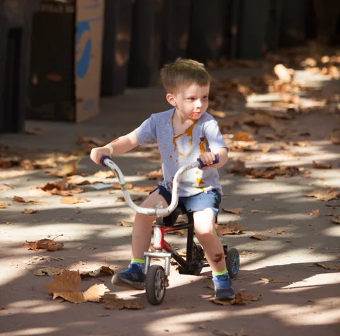 A boy rides a small trike down a shaded path.