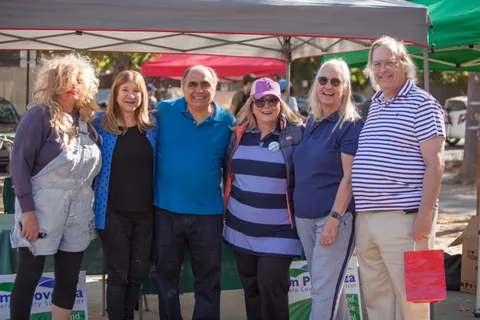 Six adults smile together under a canopy at an event booth.