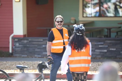 Two volunteers in orange safety vests stand near a red building.