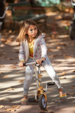 A girl rides a low trick trike through dappled shade.