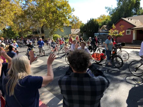 A crowd of onlookers waves toward passing riders on a downtown street.