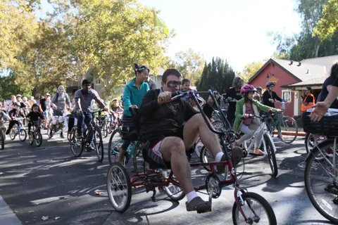 A rider on a low recumbent trike in zombie makeup leads a large pack of costumed cyclists downtown.