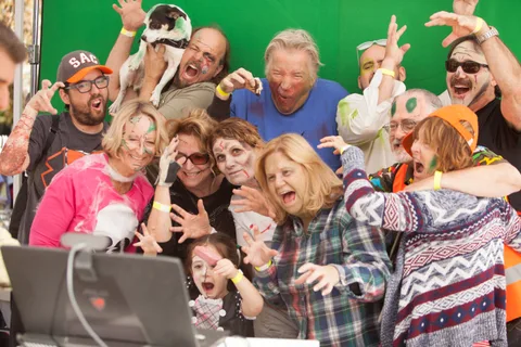 A large costumed group, including a dog, poses with monster hands in front of a green screen.