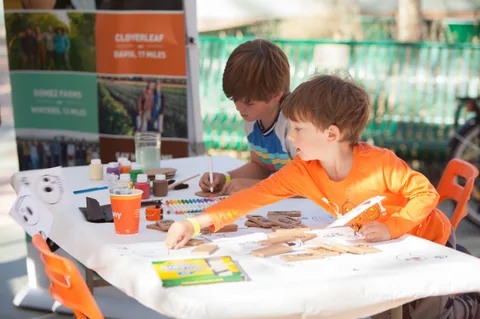 Two boys paint at the same craft table with an adult helper.