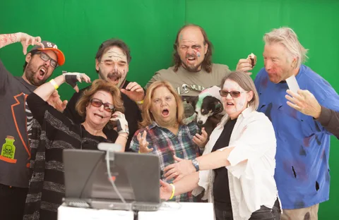A group poses excitedly in front of a green screen backdrop, motion-blurred.