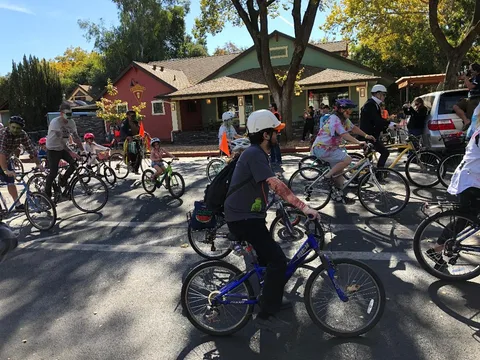 Riders on bikes cluster together on a sunlit street.