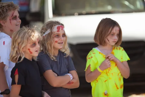 Two girls in colorful outfits and face paint stand together.