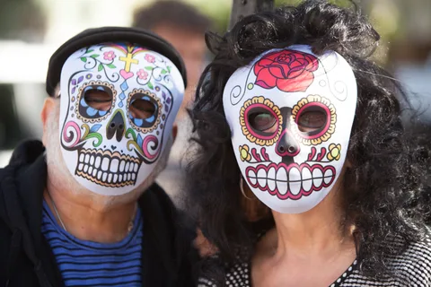 A couple wears colorful Day of the Dead sugar skull masks.