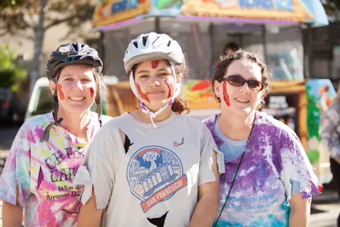 Three riders in helmets and face paint pose together smiling.