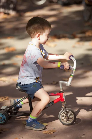 A boy in a blood-stained shirt leans playfully over his bike handlebars.