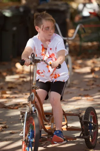 A boy with a blood-stained shirt sits on his trike looking directly at the camera.