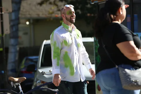 A man with green paint splattered on his white shirt walks past a woman with her back turned.