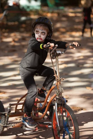 A child in a helmet and zombie face paint sits on a trike.