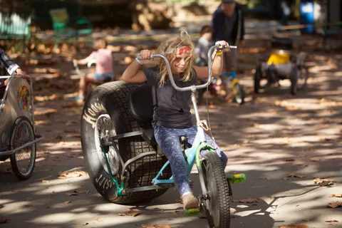 A rider pedals a big-wheeled chopper trike through the shade.