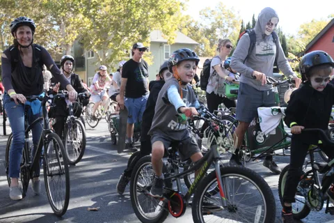 Riders including children on bikes move through dappled shade.