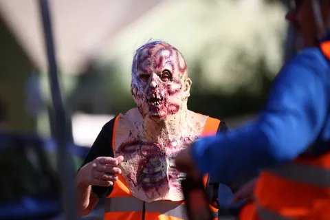 A man in an elaborate gory zombie mask and orange vest stands in soft afternoon light.
