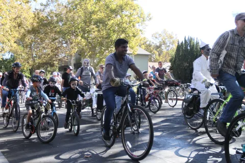 A cluster of riders on bikes pedals together on a sunlit street.