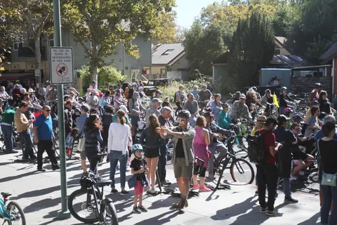 A large crowd of riders and families gathers with bikes at the park before the ride.