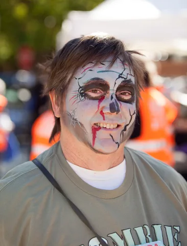 A man grins with detailed skull face paint and dark eye makeup.