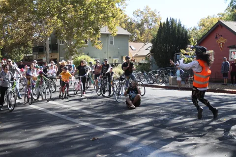 A volunteer in an orange vest waves near a group of riders gathering.