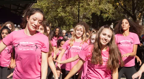 A smiling dancer in a Mirror Image Dance Company shirt strikes a zombie-dance pose in the sun.