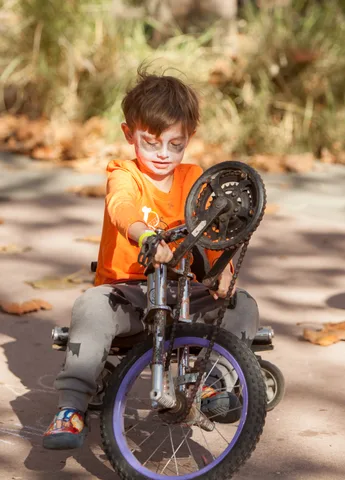 A boy in an orange shirt works on a small trick bike.