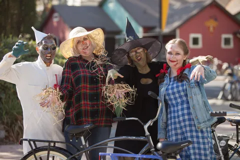A scarecrow and a ghoul in costume stand beside a parked bike.