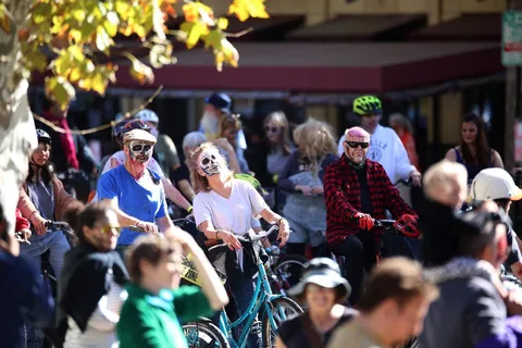 A cluster of costumed riders and pedestrians move past a downtown storefront.