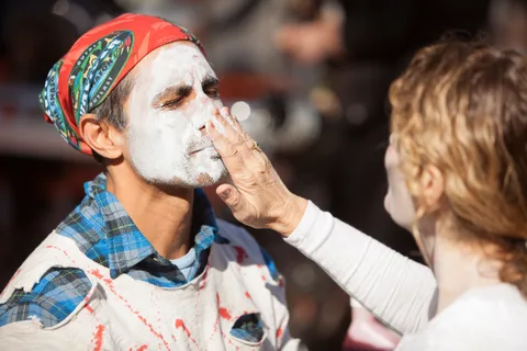 The same man continues to have white face paint applied.