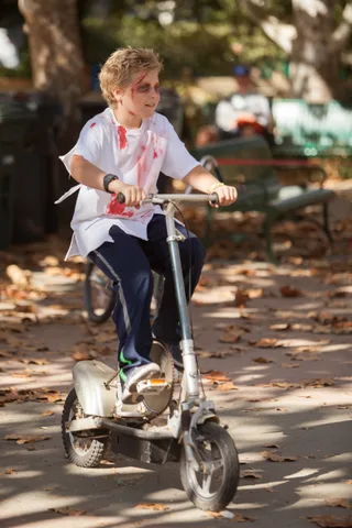 A boy with a blood-stained shirt sits on a bike smiling toward the camera.