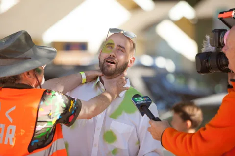A man in face paint speaks into a microphone held by an interviewer.