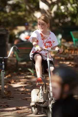 A girl with a blood-stained shirt smiles brightly while riding her bike.